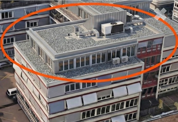A multi-story building with a flat roof, visible air conditioning units, and surrounding structures.