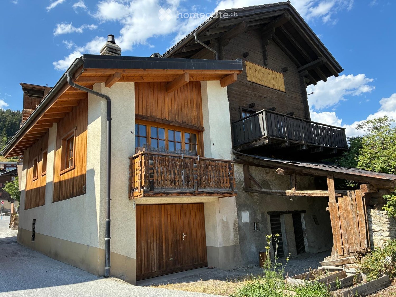 A two-story wooden house with balconies, large windows, and a garage entrance.