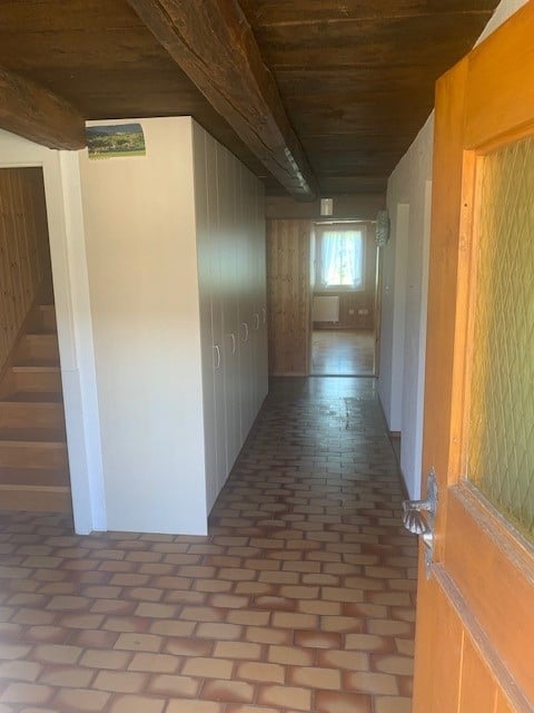 Empty hallway with wooden ceiling beams, brick flooring, white cabinetry, and a staircase leading upwards.