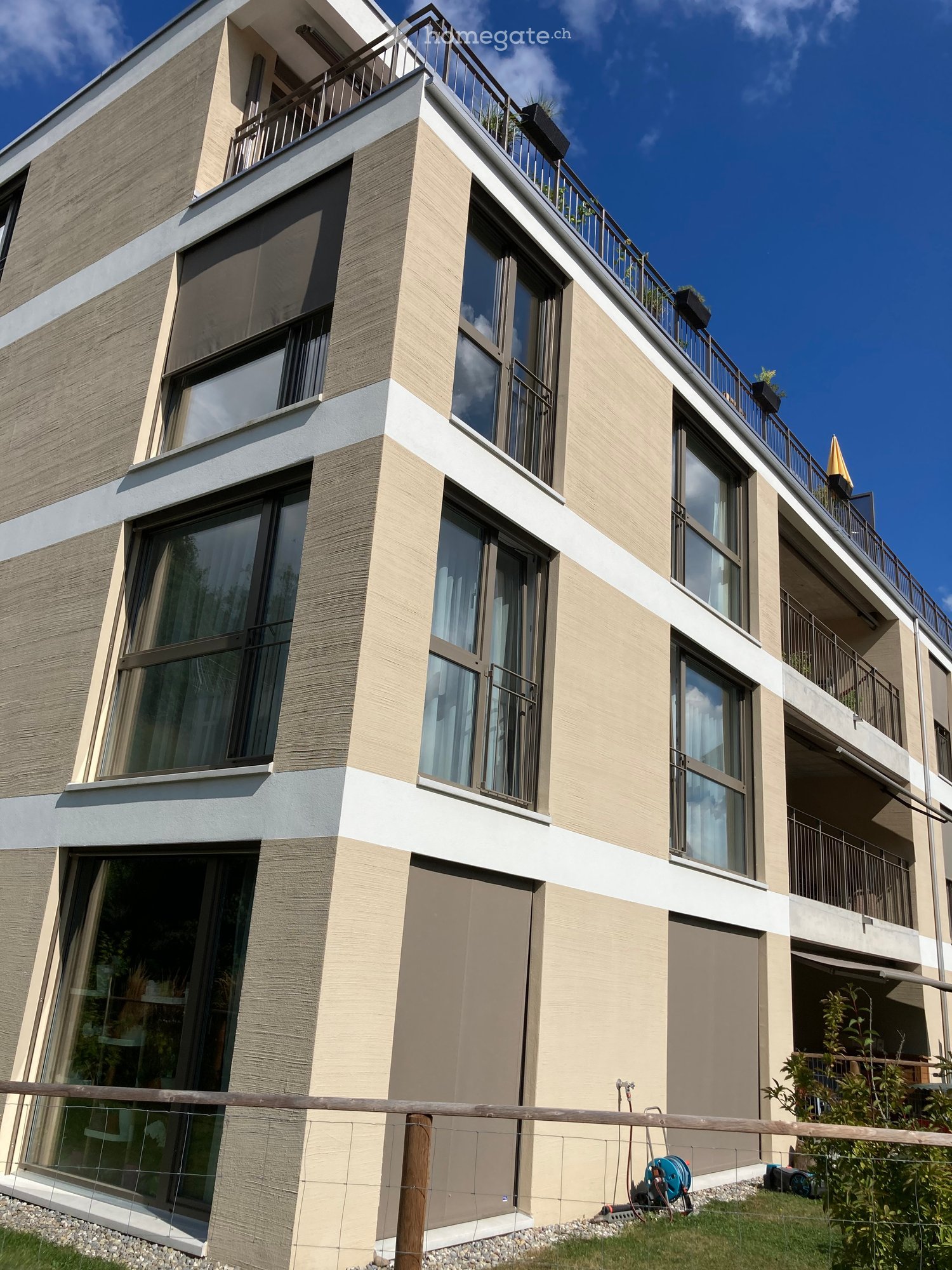 Modern multi-story building with large windows, balconies, and a mix of beige and grey exterior finishes.
