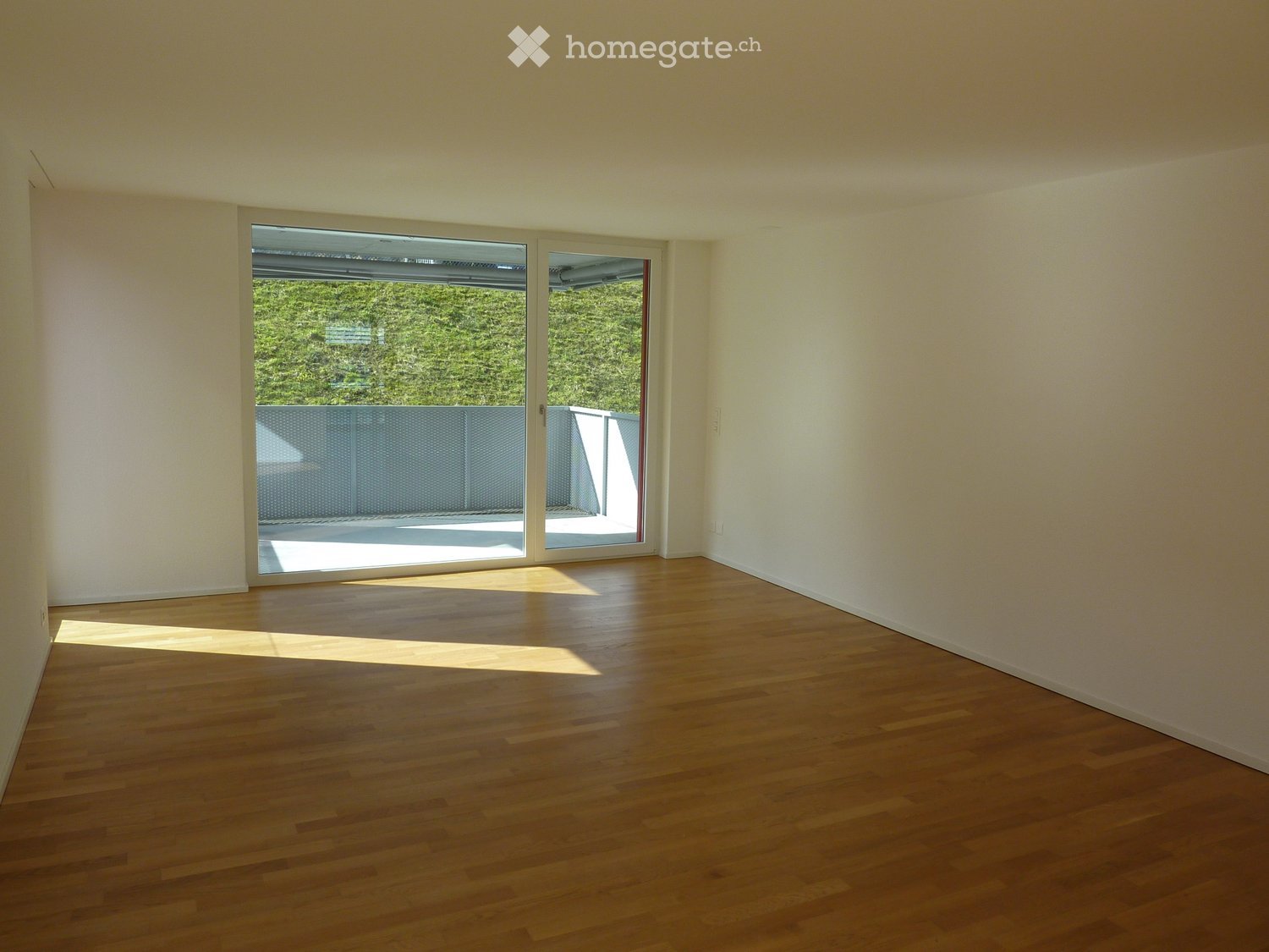 Empty room with wooden flooring and large sliding glass doors leading to a balcony or terrace area.