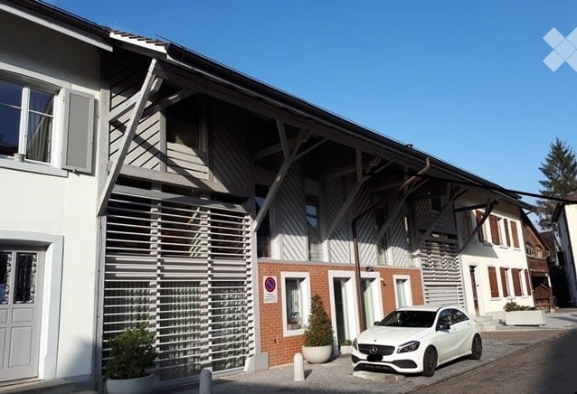 Modern multi-unit building with white and grey facade, large windows, and a parked car in front.