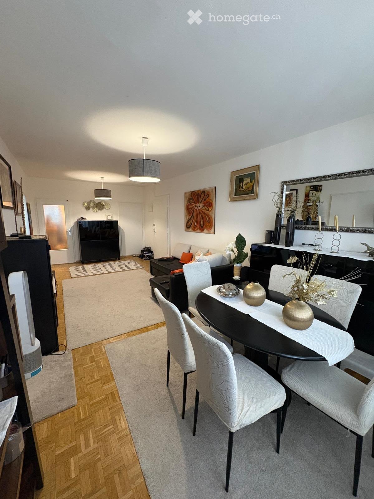 Modern living and dining area with a sofa, ottoman, dining table with chairs, decorative vases, artwork, and lamps.
