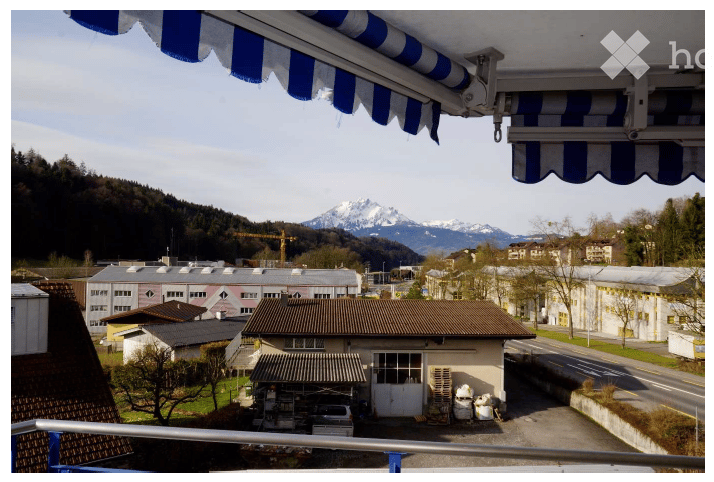Balcony with a view of a town, industrial buildings, and mountains in the background. The balcony has a blue and white striped awning.