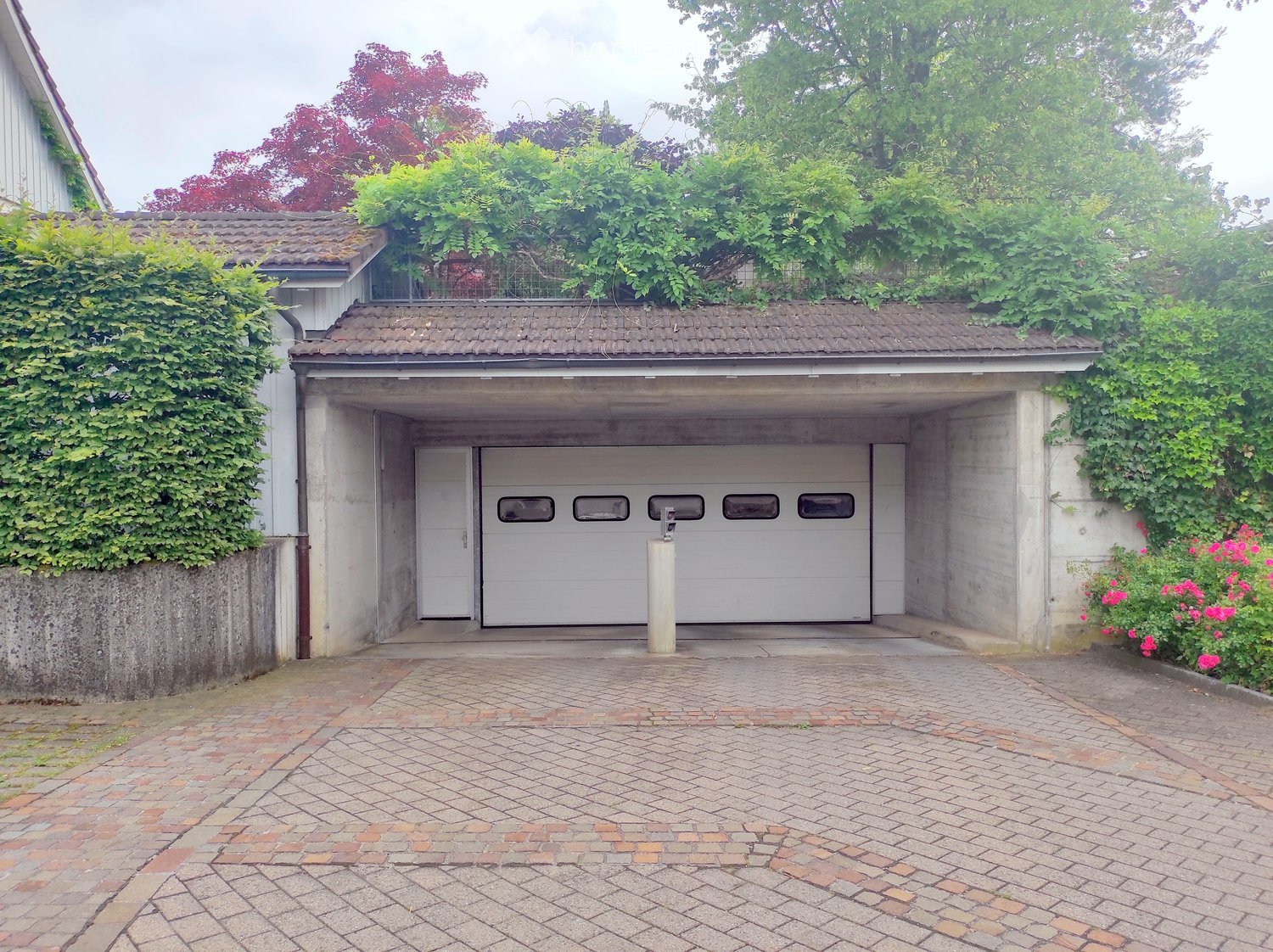 Garage with a tiled roof, surrounded by greenery and a paved driveway.