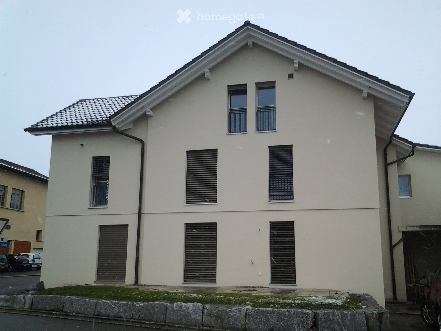 Two-story house with beige exterior, multiple windows, and a tiled roof.