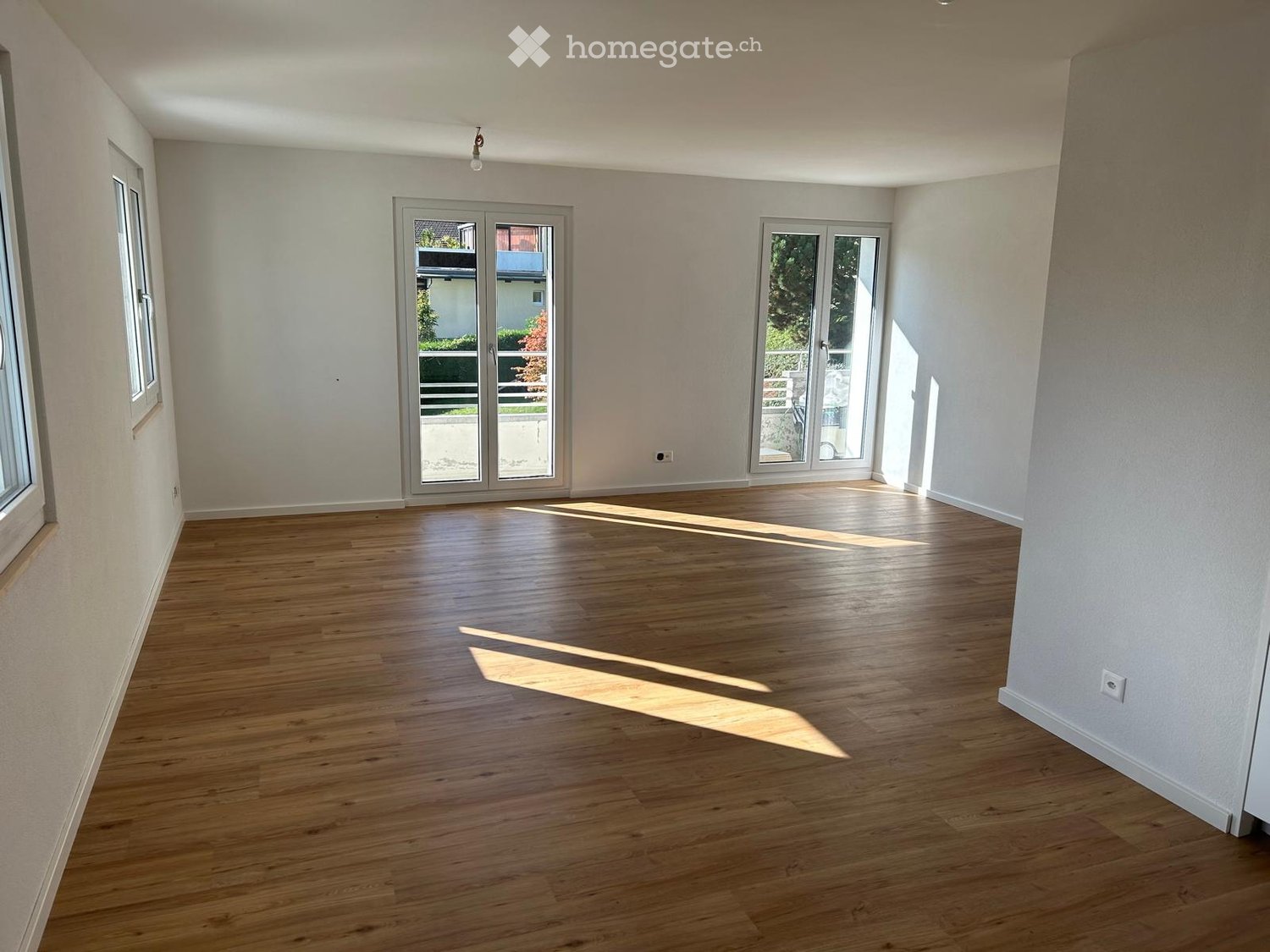 Empty room with wooden flooring, white walls, large windows, and sliding glass doors leading to an outdoor area.