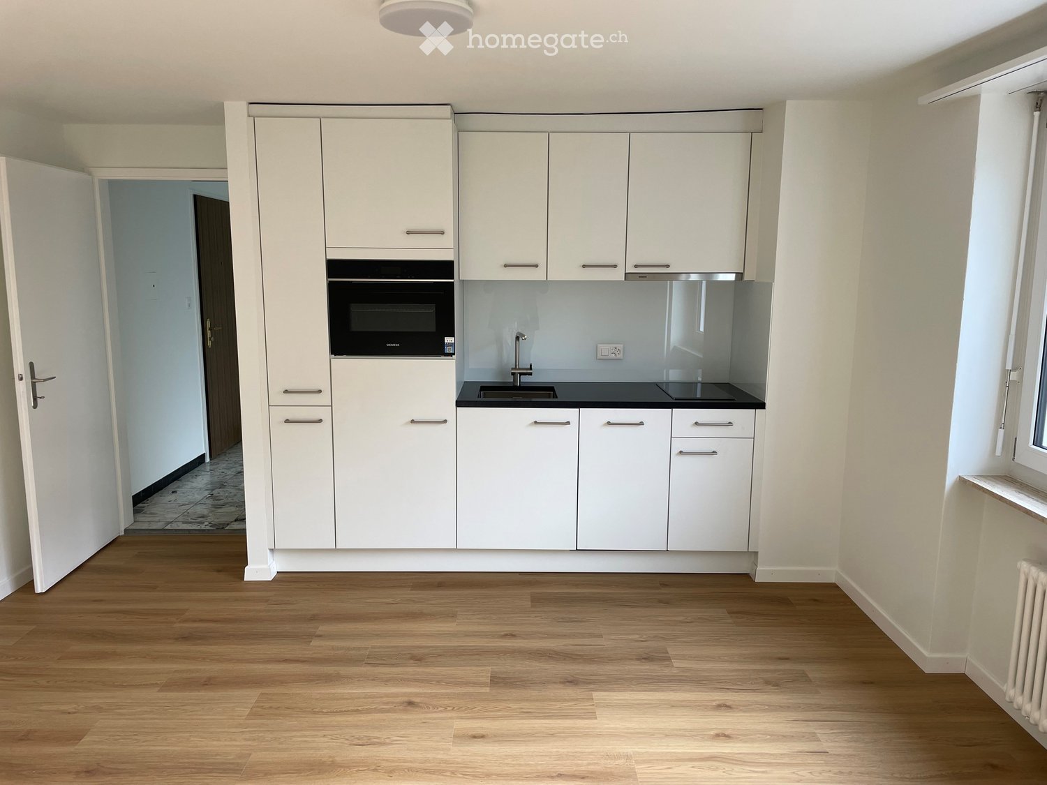 Modern kitchen with white cabinets, a built-in oven, a sink with a faucet, and wooden flooring.