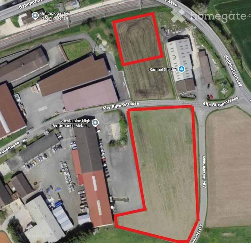 Aerial view of an industrial area with multiple buildings, parking lots, and surrounding roads. Red outlines highlight two plots of land.