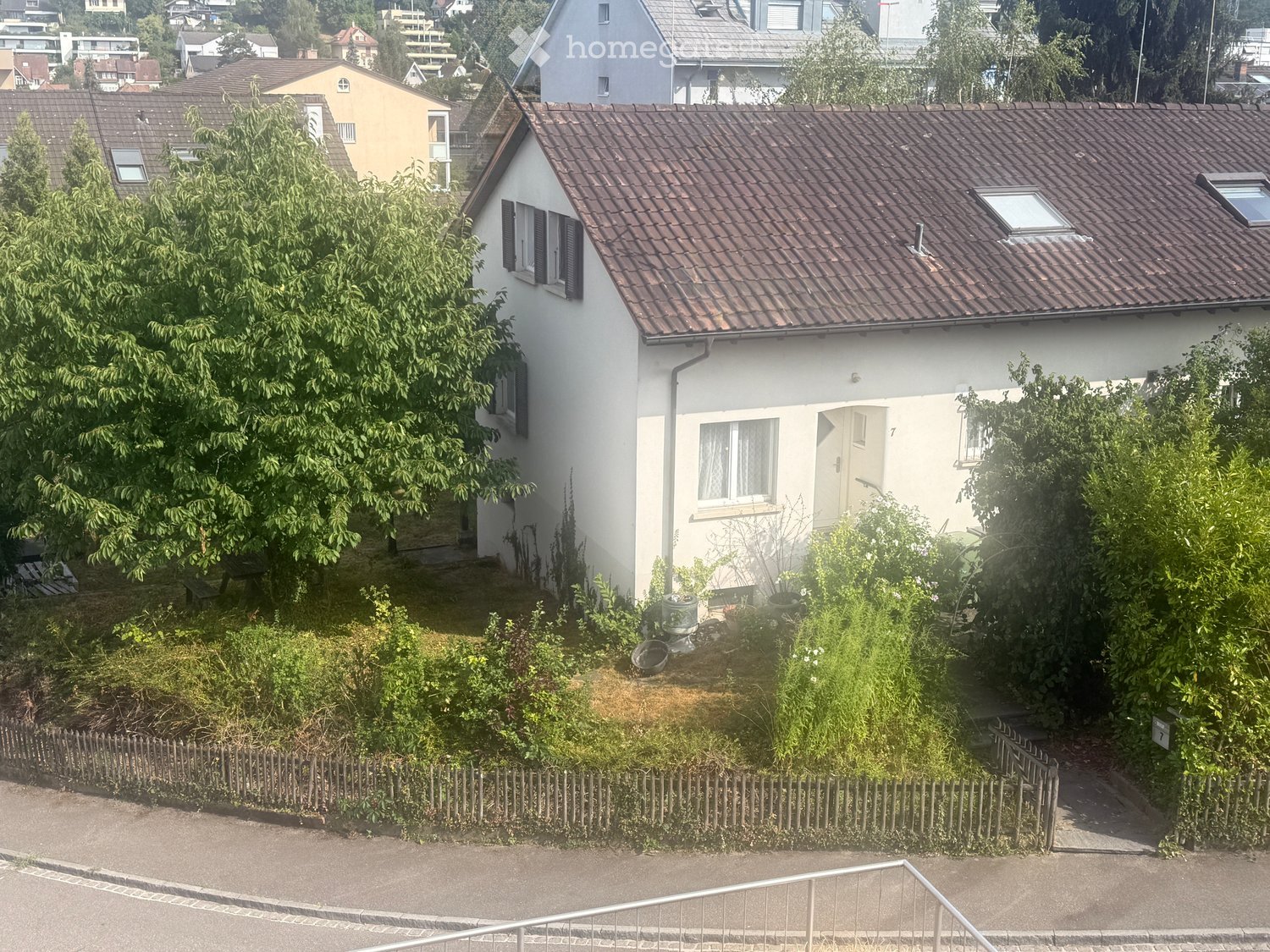 Single-family house with a tiled roof, white exterior, and small garden area surrounded by a wooden fence.