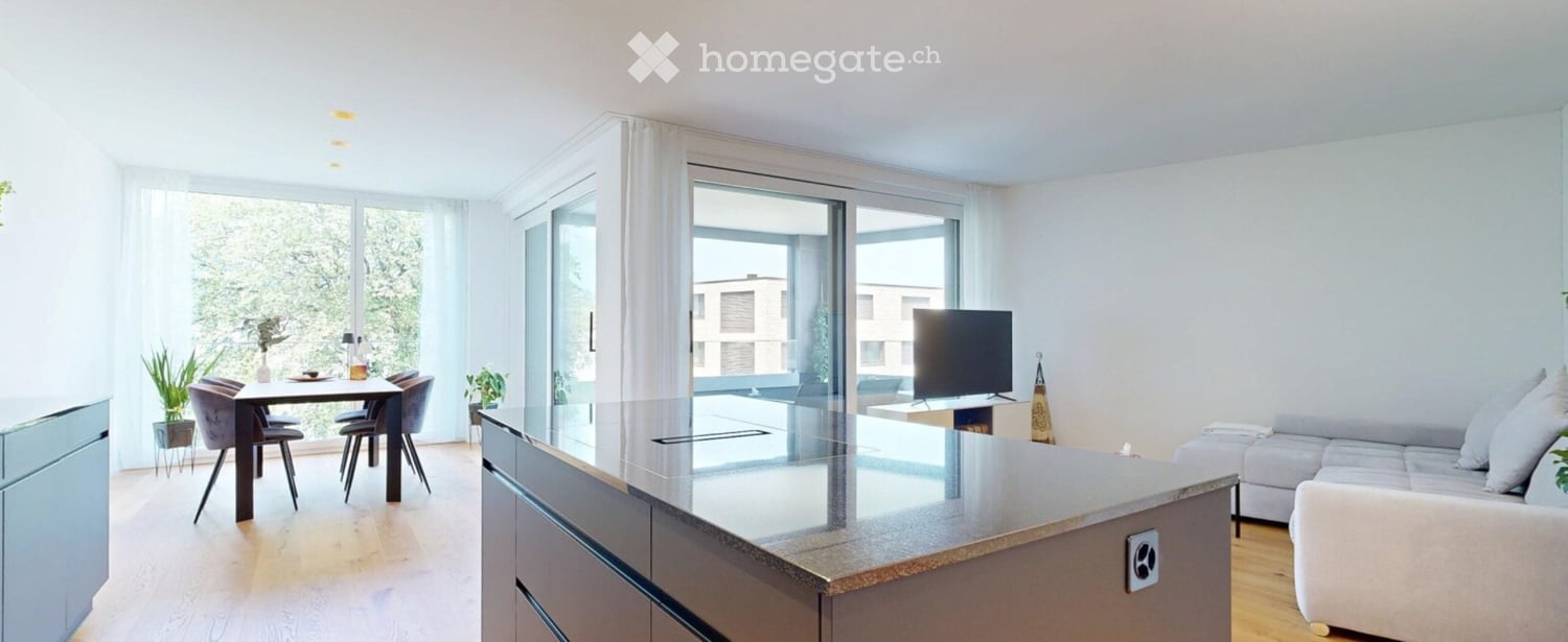 Modern open-plan living and dining area with large windows and a view, featuring a sofa, coffee table, dining table, chairs, and a television.