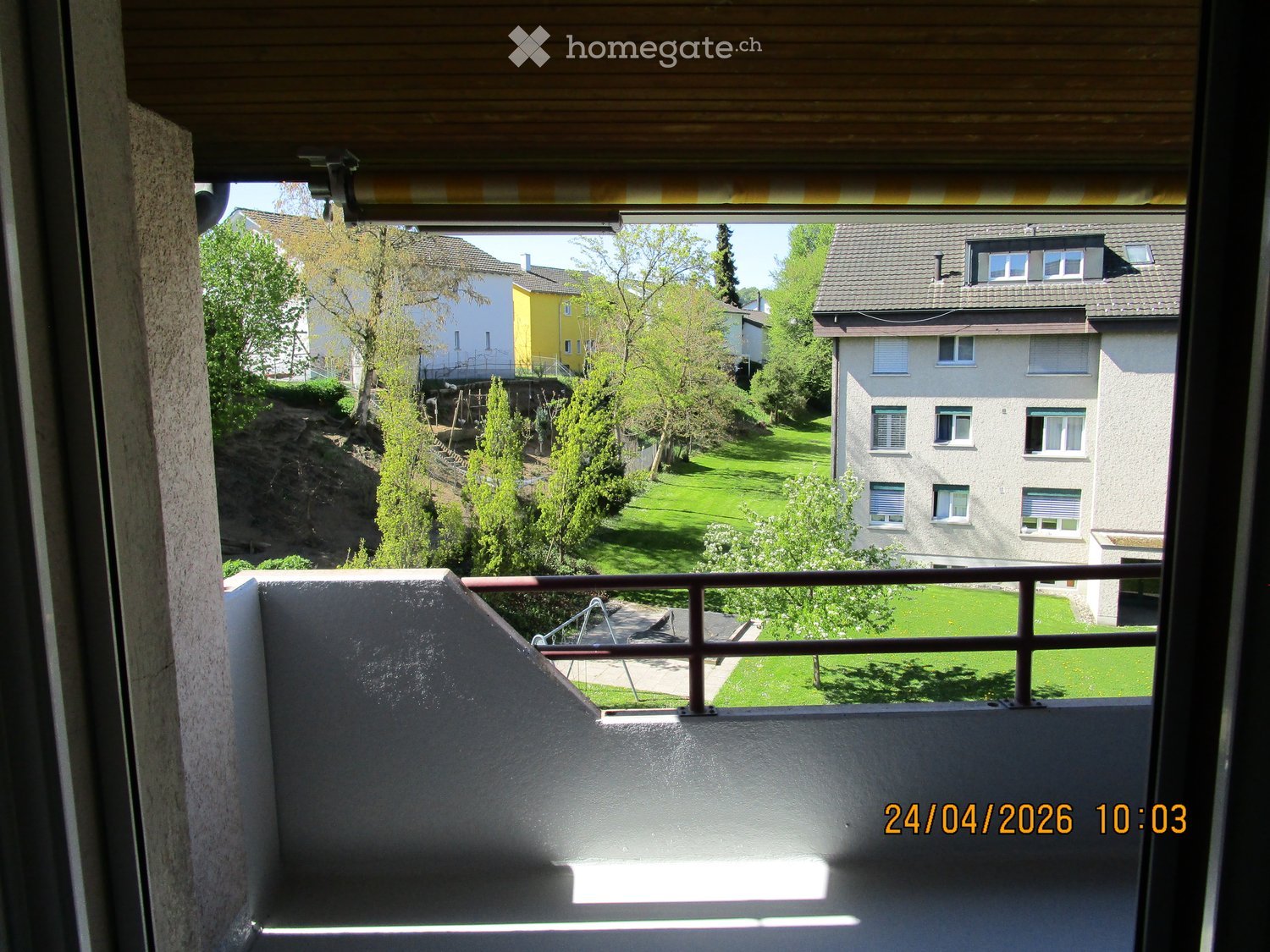 Balcony / Terrace. Balcony with metal railing overlooking a green lawn, trees, and neighboring buildings.