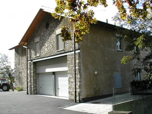Two-story stone building with a garage entrance, multiple windows, and a sloped roof.