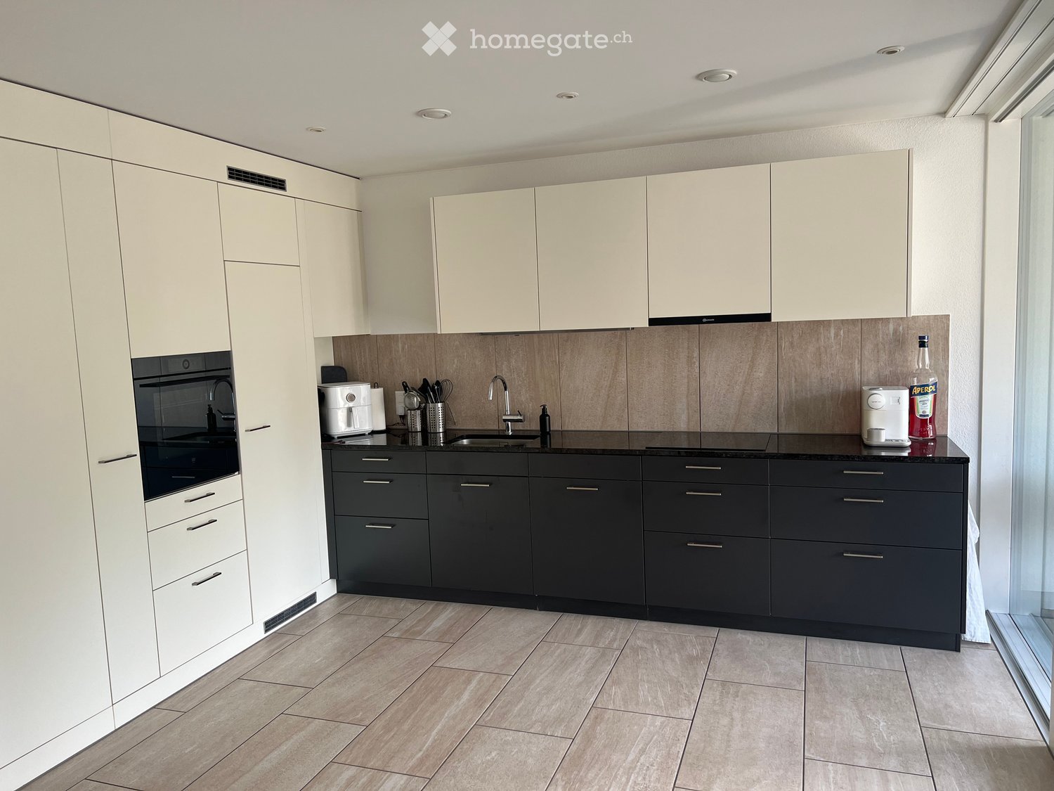 Modern kitchen with white and black cabinets, a central island, and various appliances including an oven, sink, and coffee maker.
