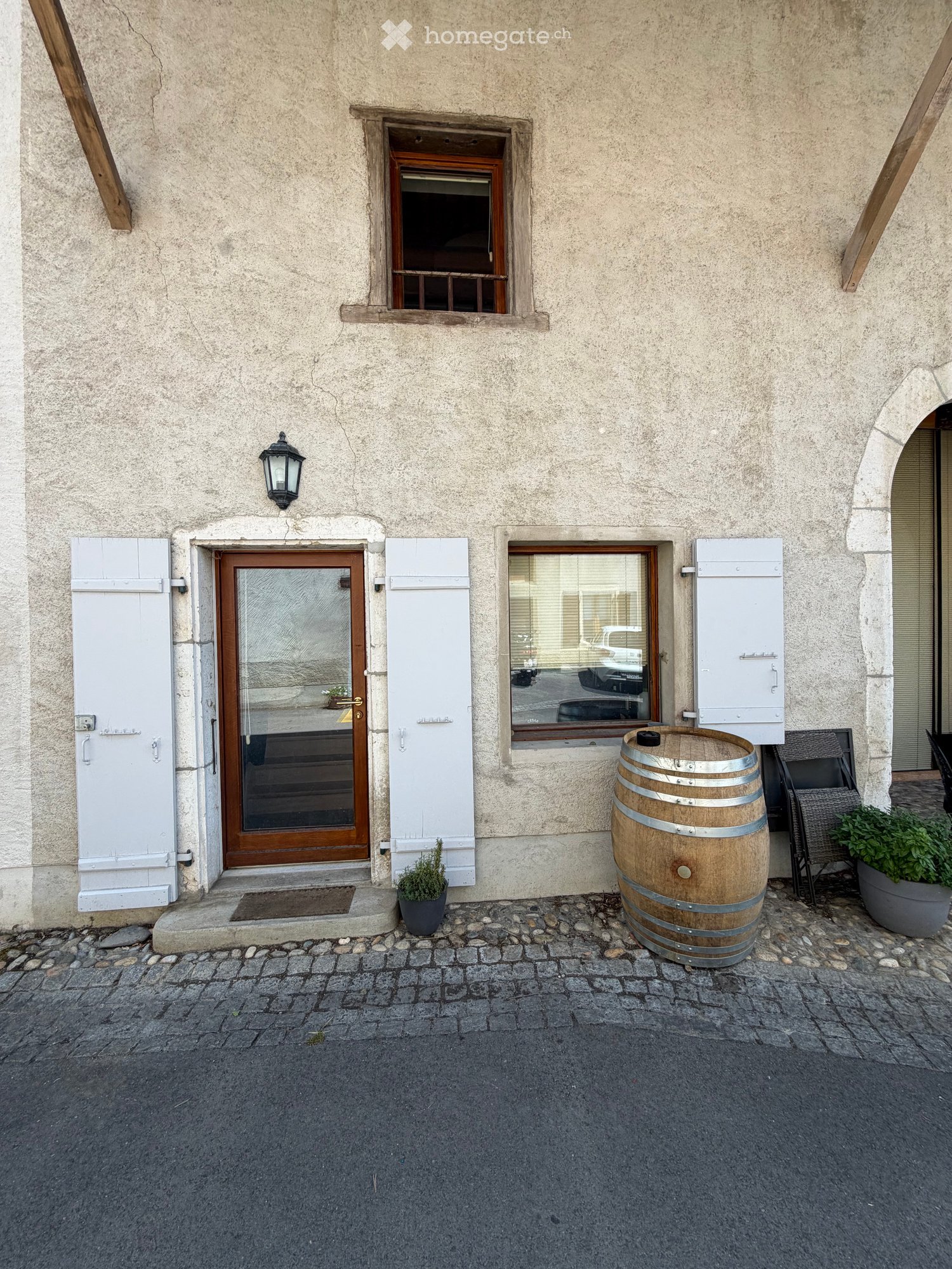 Facade of a building with a wooden door, windows, a barrel, and potted plants.
