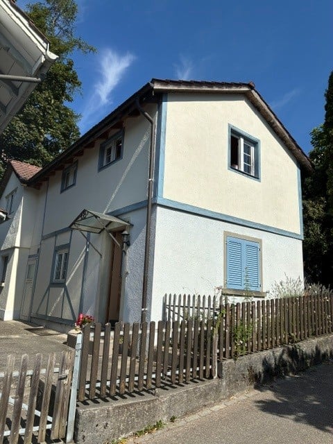 Two-story house with white siding, blue shutters, and a wooden fence in front.