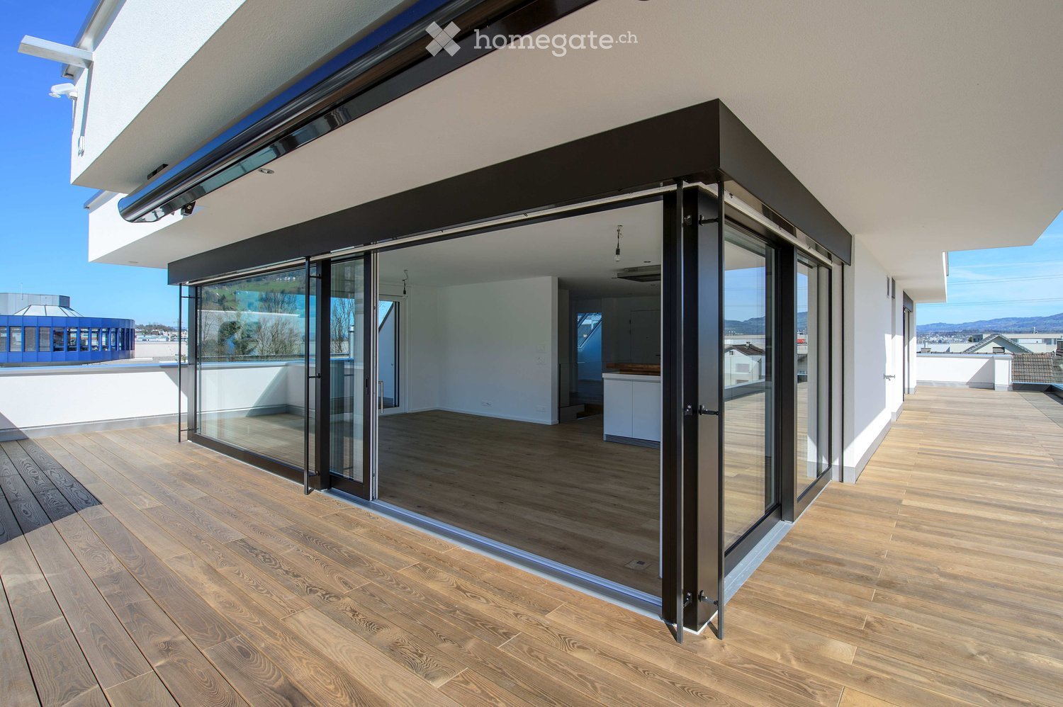 Modern balcony with wooden flooring, large glass sliding doors, and a view of the city and mountains.