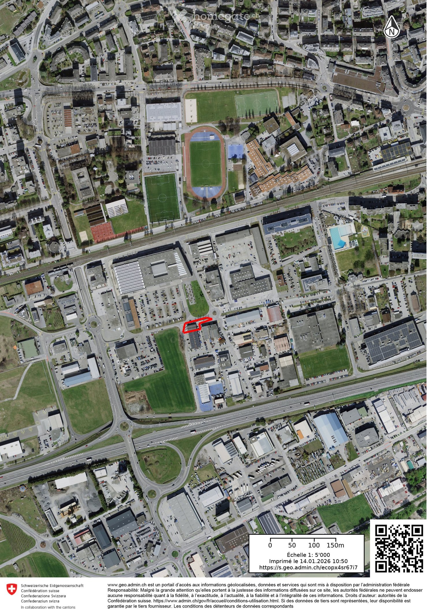 Aerial view of a residential and commercial area with multiple buildings, parking lots, green spaces, and a highlighted building in red.