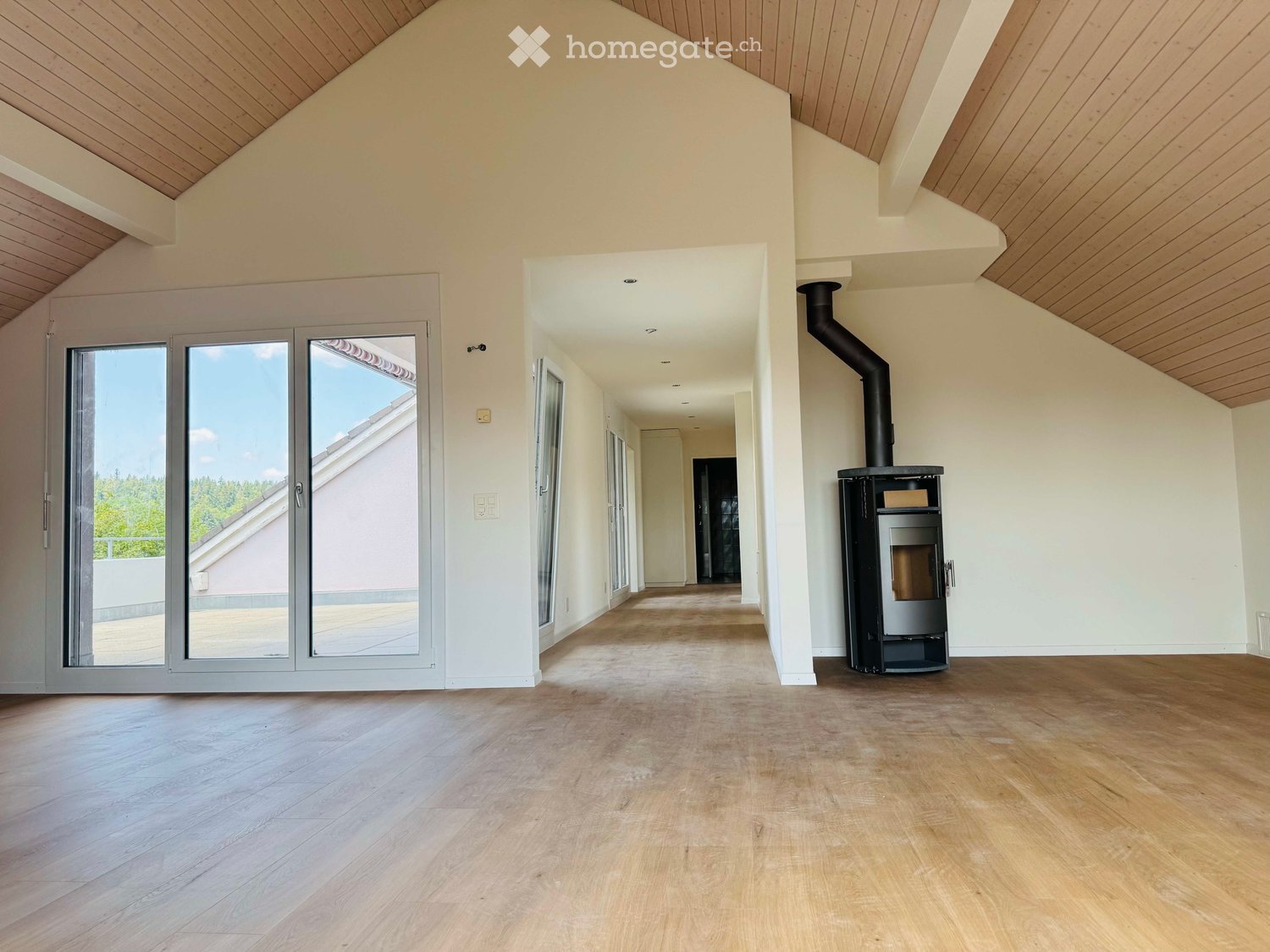Empty room with wooden flooring, white walls, and a modern fireplace. Large sliding glass doors lead to a balcony area.