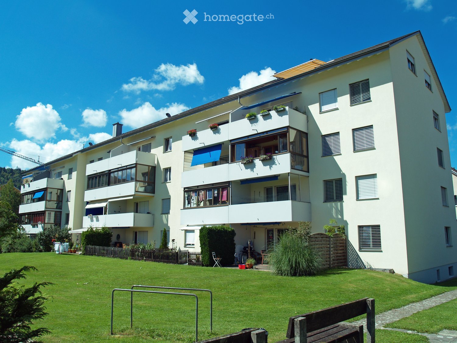Modern multi-story residential building with balconies, large windows, and a well-maintained lawn in front.
