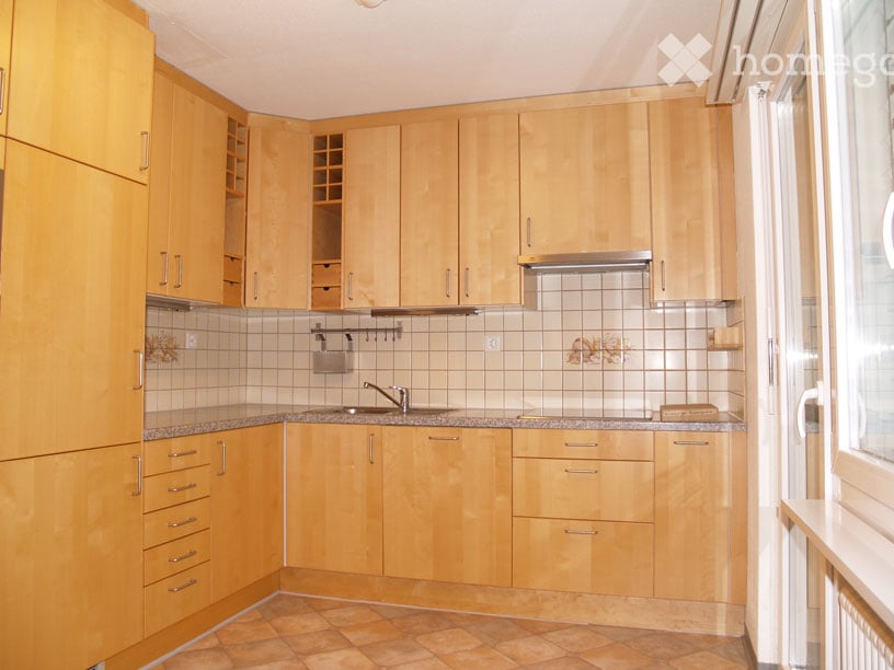 Bright kitchen with light wooden cabinets, granite countertops, and tiled backsplash. Features a sink with a modern faucet and built-in storage drawers.