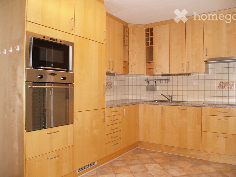 Modern kitchen with light wooden cabinets, stainless steel oven and microwave, granite countertops, and tiled backsplash.