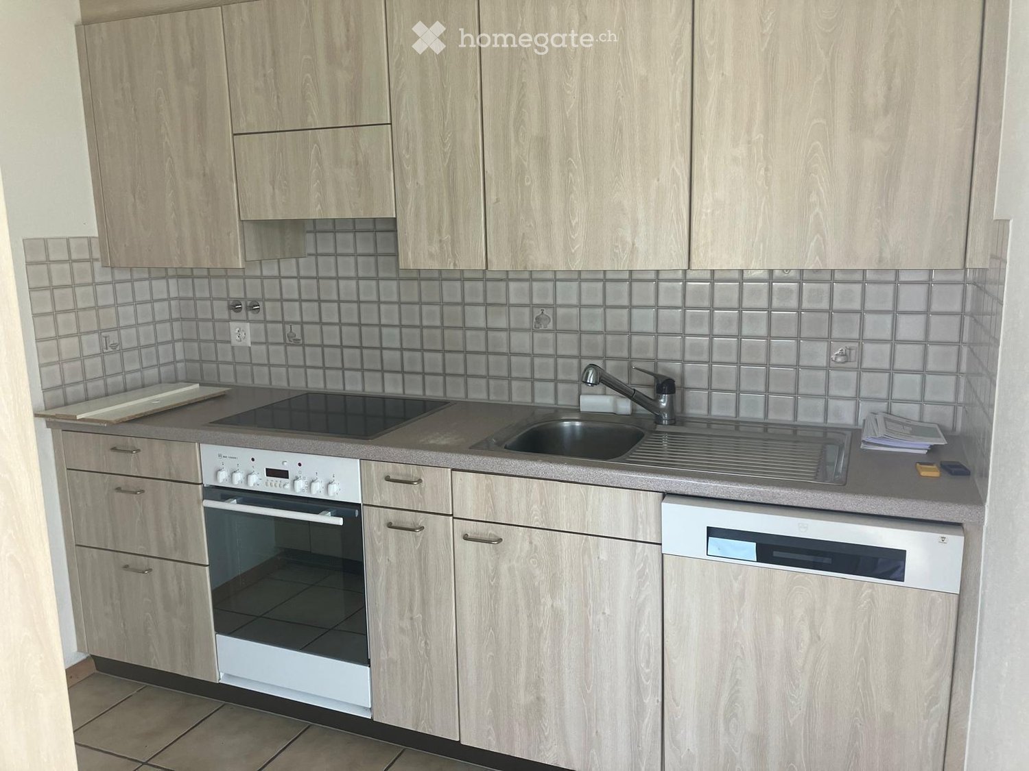 Modern kitchen with light wood cabinets, stainless steel sink, oven, and dishwasher.