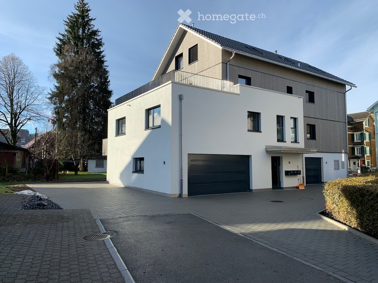 Modern two-story house with white and grey exterior, large garage, and balcony on the upper floor.