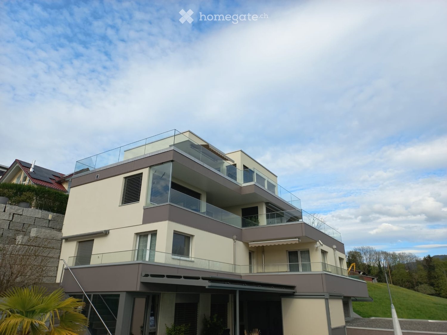 Modern two-story house with large glass balconies and a flat roof, featuring a combination of beige and brown exterior walls.