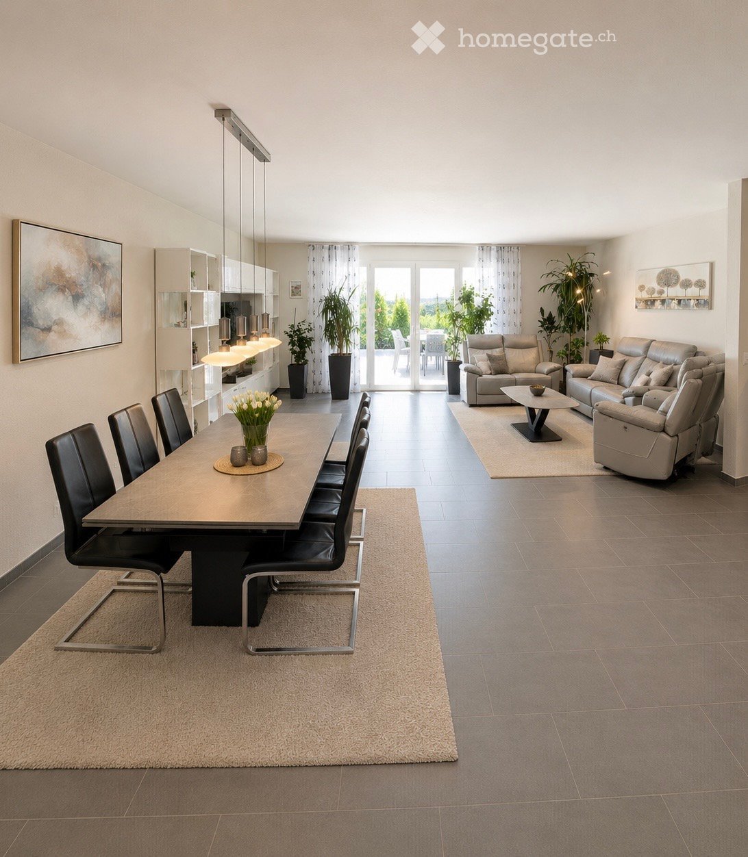 Open-plan living and dining area with modern furniture, pendant lights, and large windows leading to a balcony.