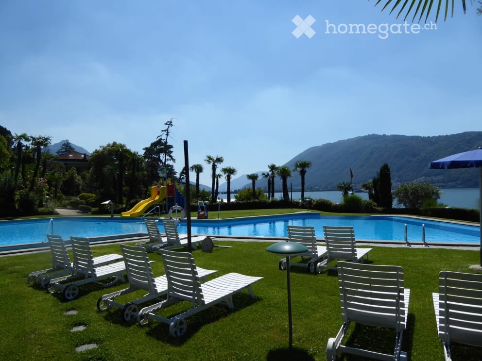 Outdoor area with a swimming pool, lounge chairs, umbrellas, and a view of a lake and mountains.