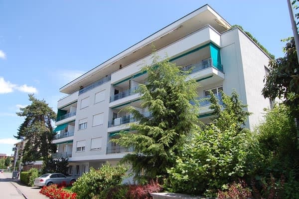 White apartment building, modern architecture, many windows, balconies, car parked in front, surrounded by greenery