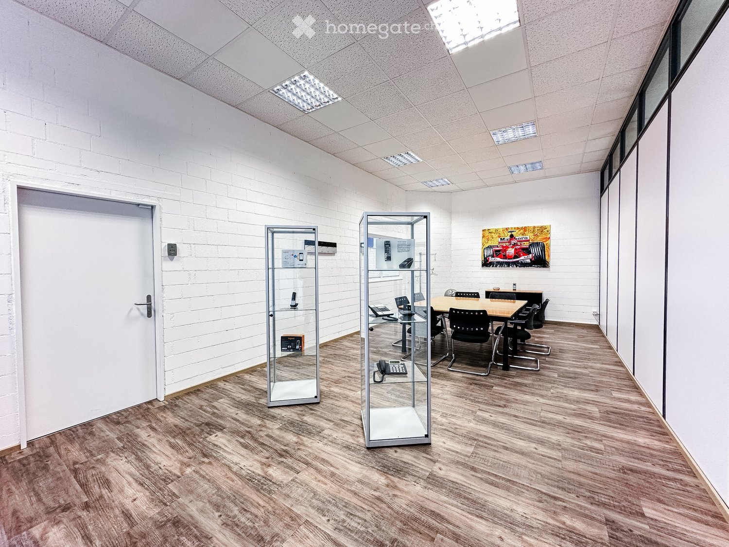 empty room, wooden floor, meeting table, display cases, white walls, ceiling lamps