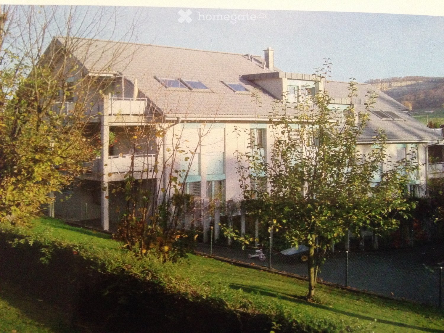 Modern two-story house with solar panels on the roof, multiple balconies, and a well-maintained lawn.