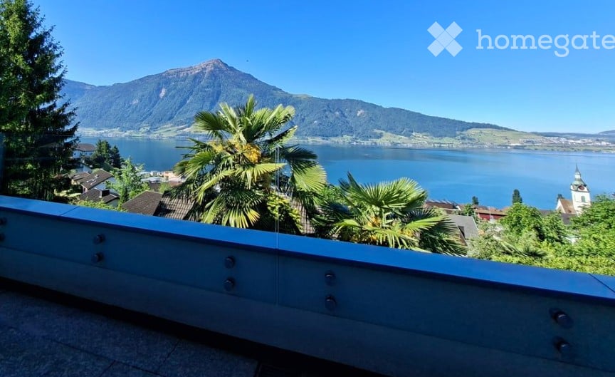 Balcony with a scenic view of a lake and mountains, surrounded by palm trees and greenery.