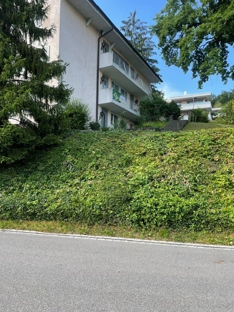 Multi-story apartment building with balconies, situated on a raised ground floor surrounded by greenery.