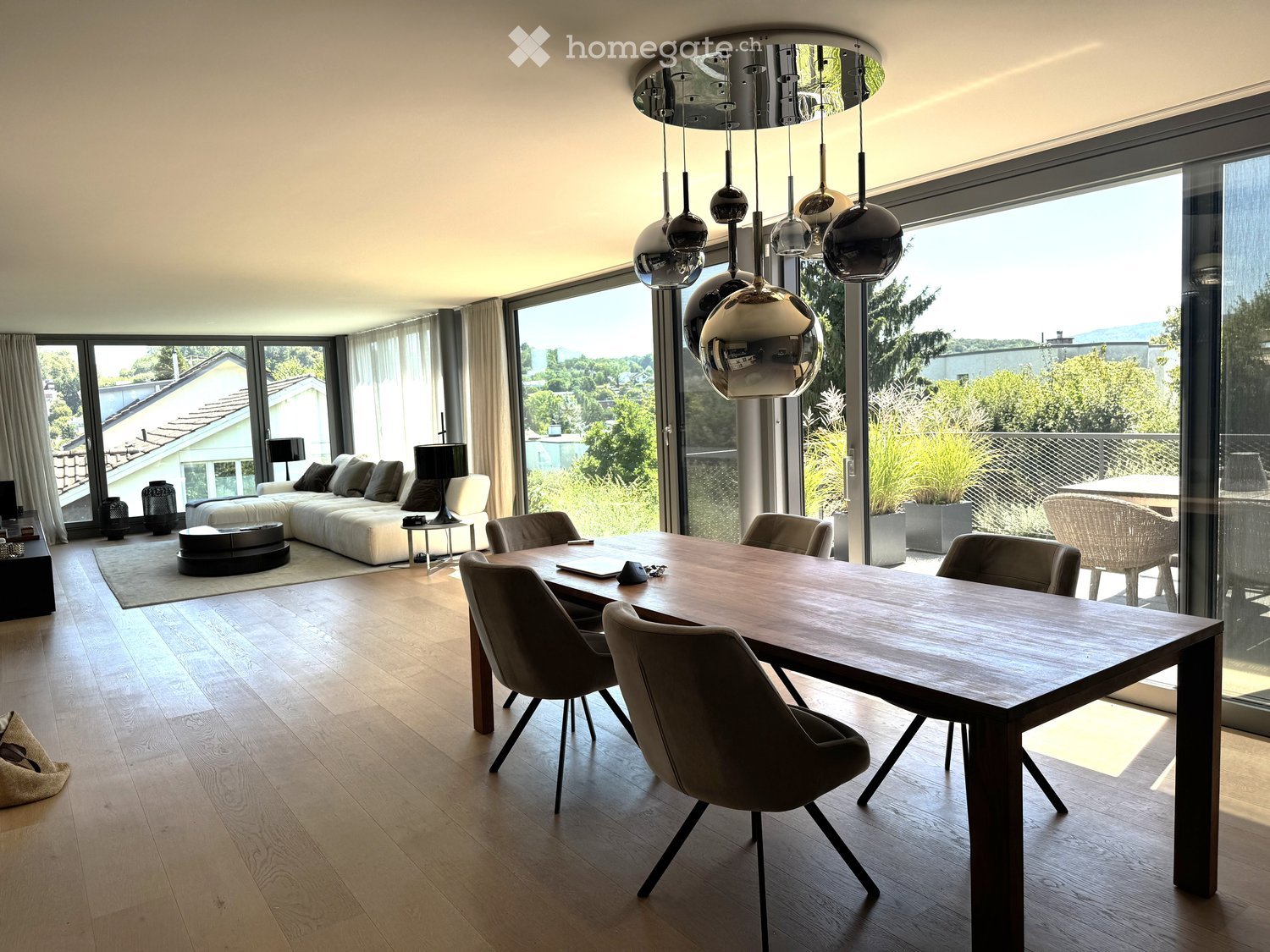 Open-plan living and dining area with large windows offering a scenic view, modern furniture including a sofa, coffee table, dining table, and chairs.