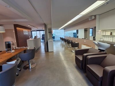 Modern reception area with a reception desk, chairs, tables, and a screen. The space features a clean, contemporary design with a polished concrete floor and soft lighting.