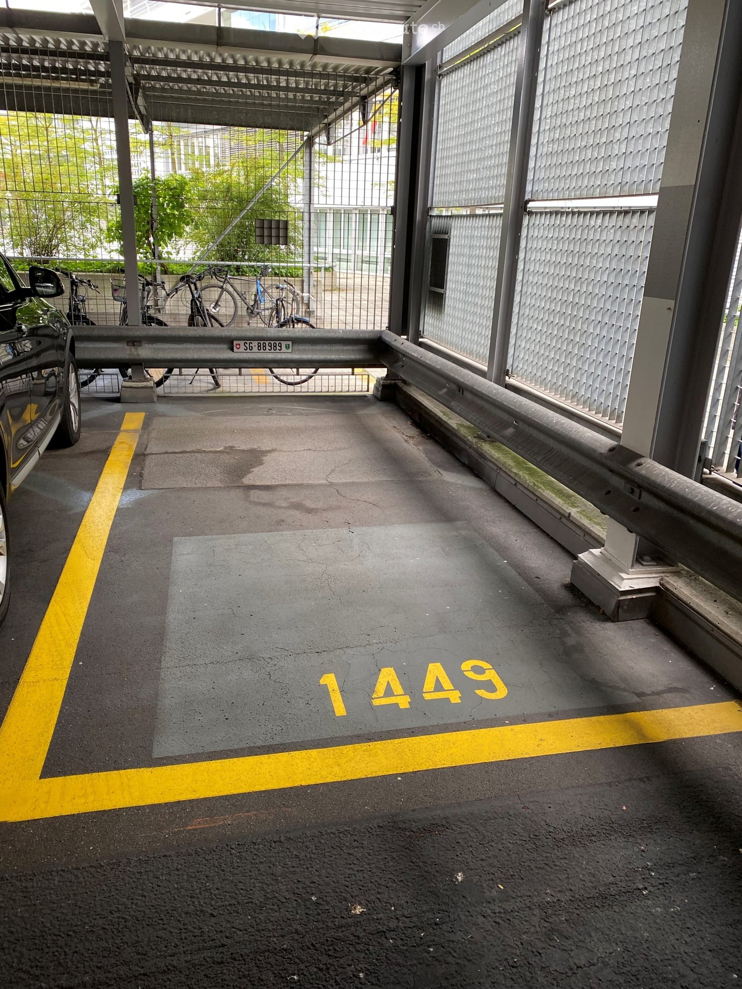 covered parking spot, number 1449, yellow parking lines, multiple bikes parked in background, grey walls and metal barriers