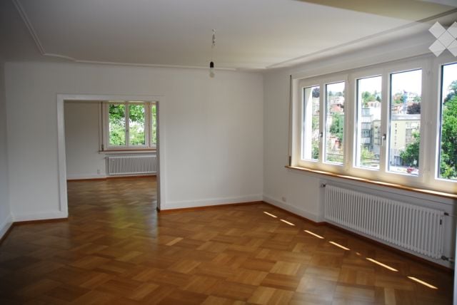 Empty room with wooden flooring, white walls, large windows, and radiators. No furniture or equipment present.