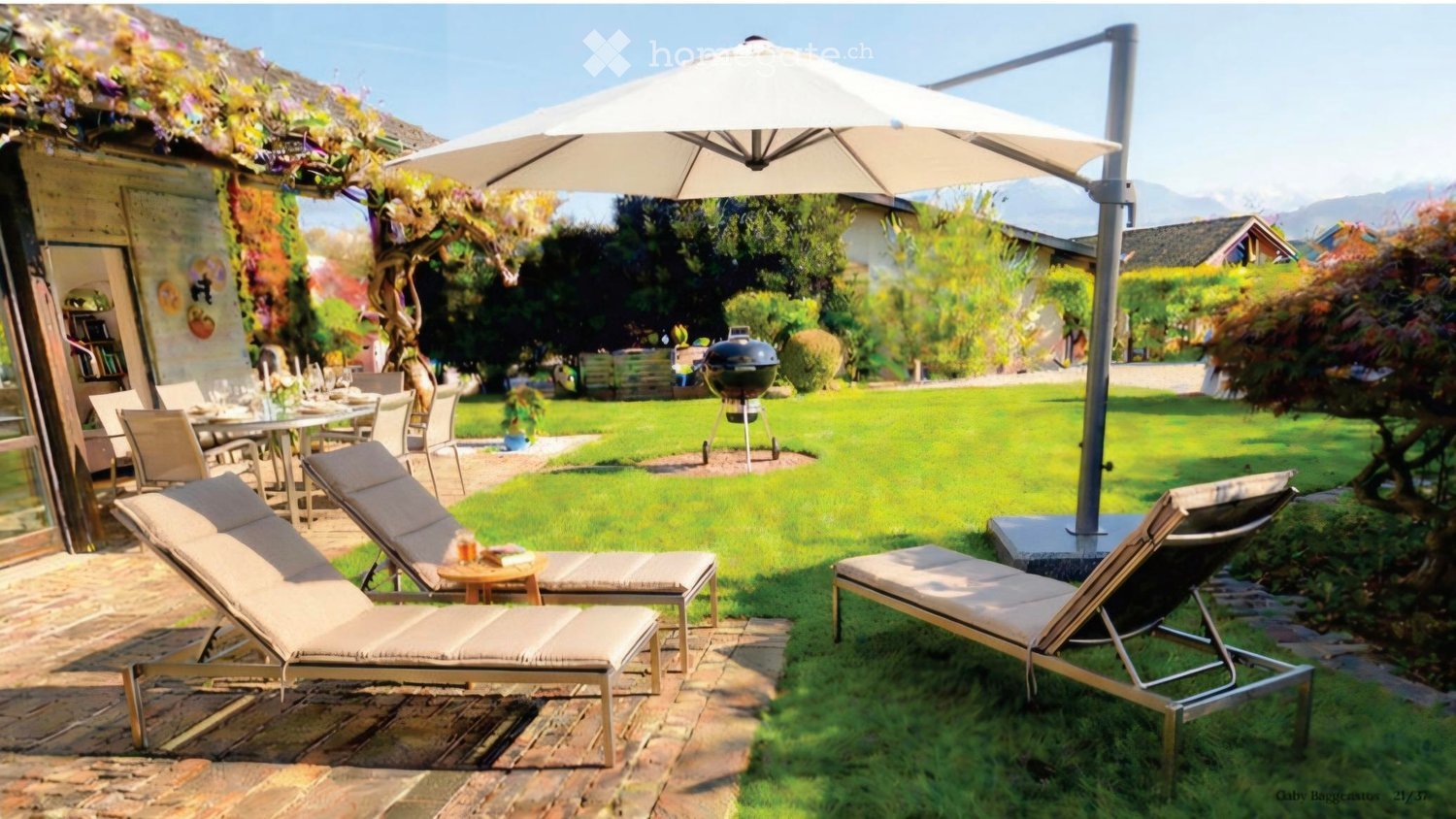 A well-maintained garden with a patio area featuring lounge chairs, a dining table with chairs, a large umbrella, and a barbecue in the background. The garden is surrounded by greenery and a house with a covered entrance.