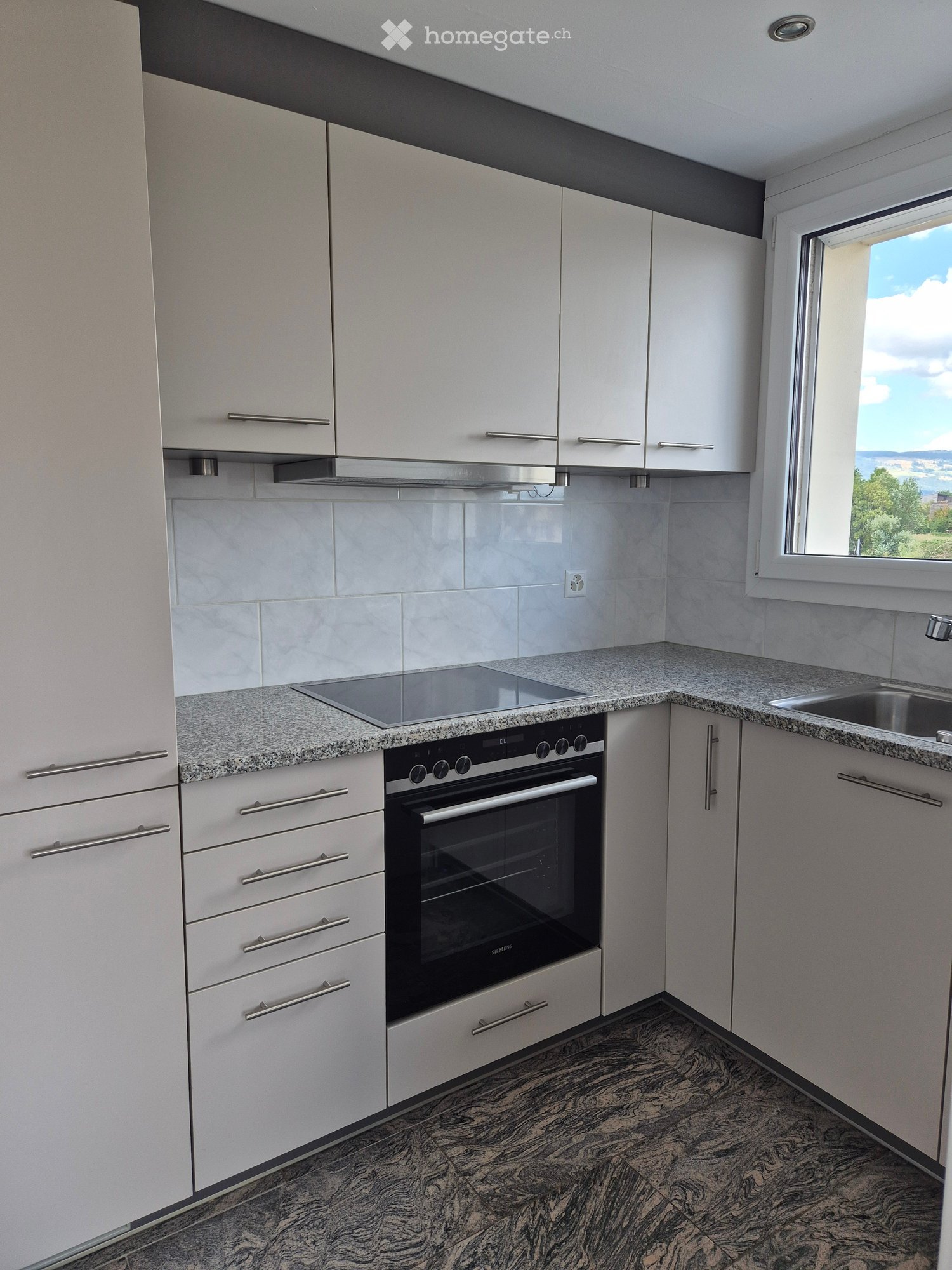Modern kitchen with white cabinets, granite countertops, and a built-in oven. Features a large window with a scenic view.