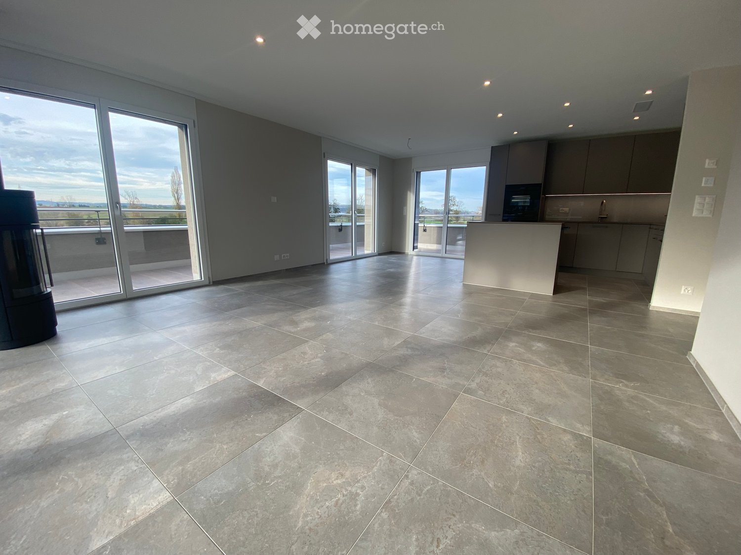 Open-plan space with large sliding glass doors leading to a balcony, tiled floor, and a small kitchen area with cabinets and a countertop.
