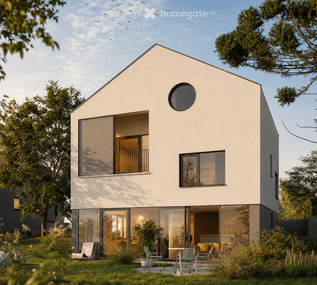 Modern single-story house with white exterior, large windows, and a balcony. The house features a contemporary design with a flat roof and a circular window on the upper level. The surrounding area includes a well-maintained garden with outdoor seating an
