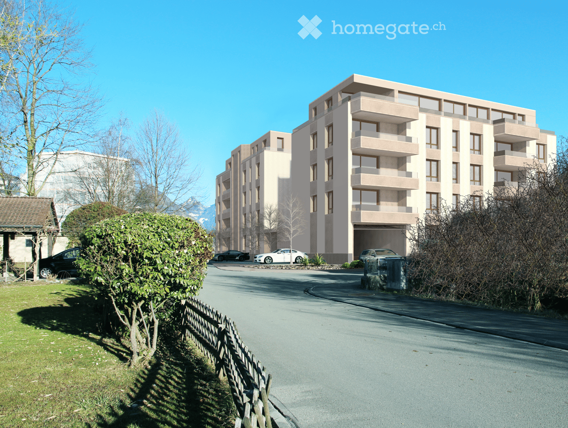 Modern multi-story residential building with balconies and a covered garage entrance, surrounded by a landscaped area with a wooden fence and parked cars.