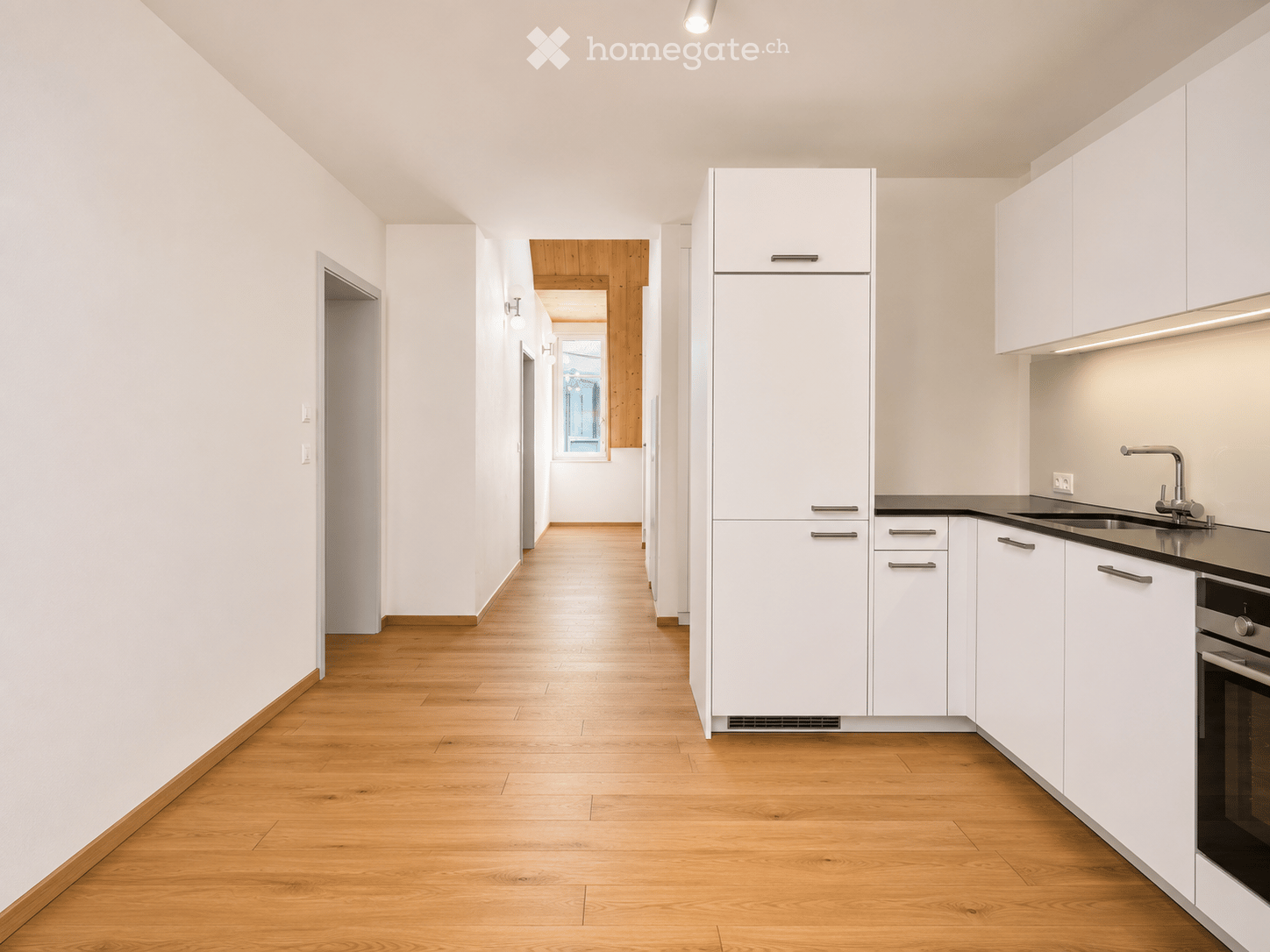 Modern kitchen with white cabinets, wooden flooring, and stainless steel appliances including a refrigerator, sink, and oven.