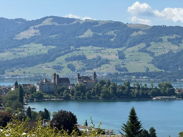 A historic castle sits on an island in a lake, surrounded by lush green hills and a clear blue sky.
