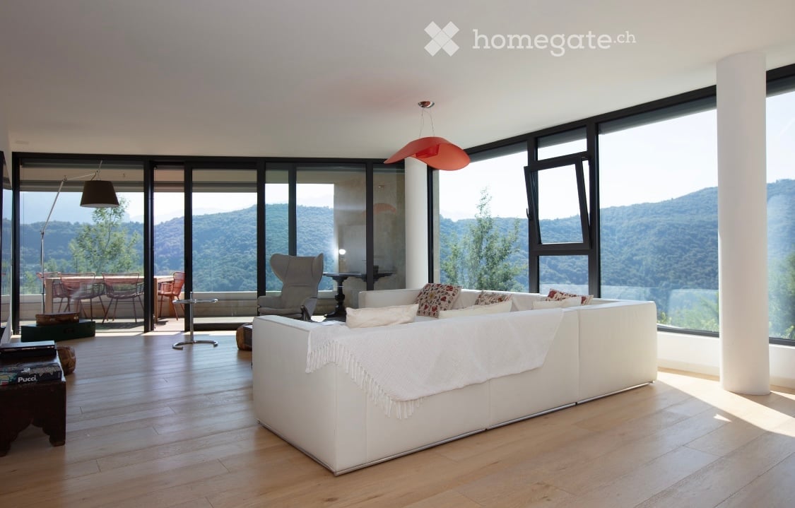 modern living room with large windows, white sofa, wooden floor, outdoor terrace with table and chairs, mountains in the background