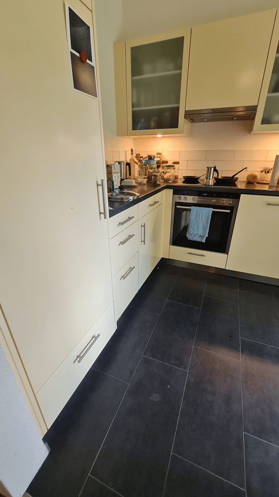 Modern kitchen with white cabinets, black tiled floor, stainless steel oven, and countertop with various kitchen items.