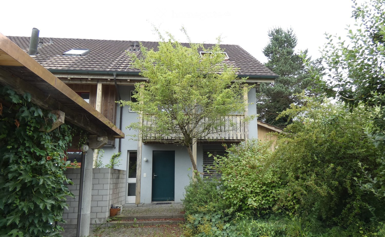 2 story house, brown roof, balcony, white walls, green door, surrounded by plants